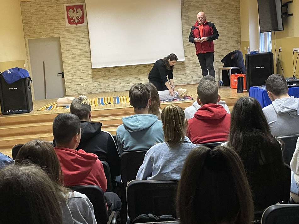 sala w szkole na ścianie polskie godło uczniownie patrzą na kobietę pochyloną nad fantomem do resuscytacji