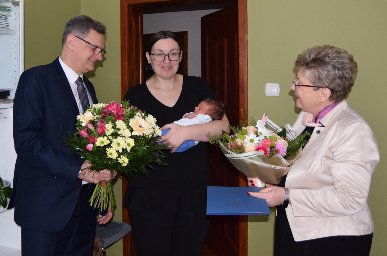 Przedstawiciele Powiatu stoją z mamą trzymająca noworodka na ręku.