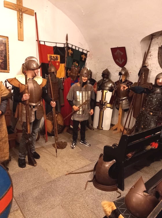 Grupa uczniów stoi w pomieszczeniu w zbroajch rycerskich.