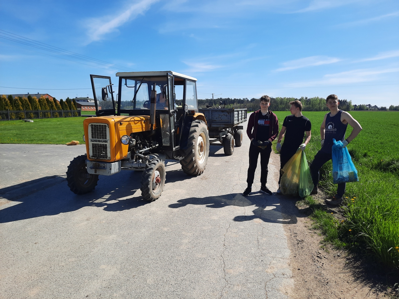 Młodzież sprząta rowy, na drodze stoi traktor