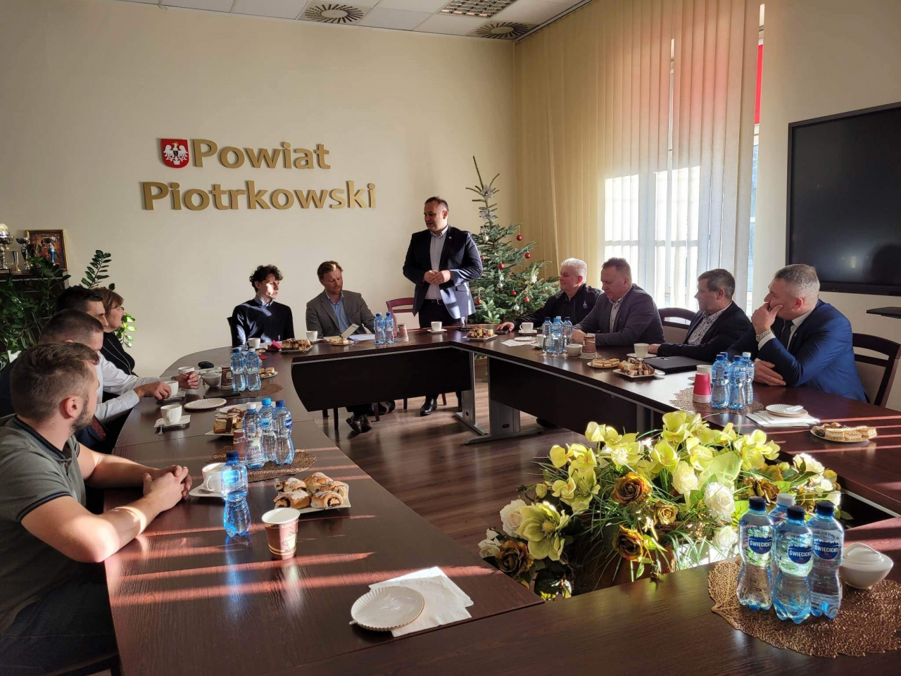 Starosta Piotr Wojtysiak podczas spotkania z delegacją Ambsaday Danii znajduje się w sali konferencyjnej Starostwa. W tle napis Powiat Piotrkowski.