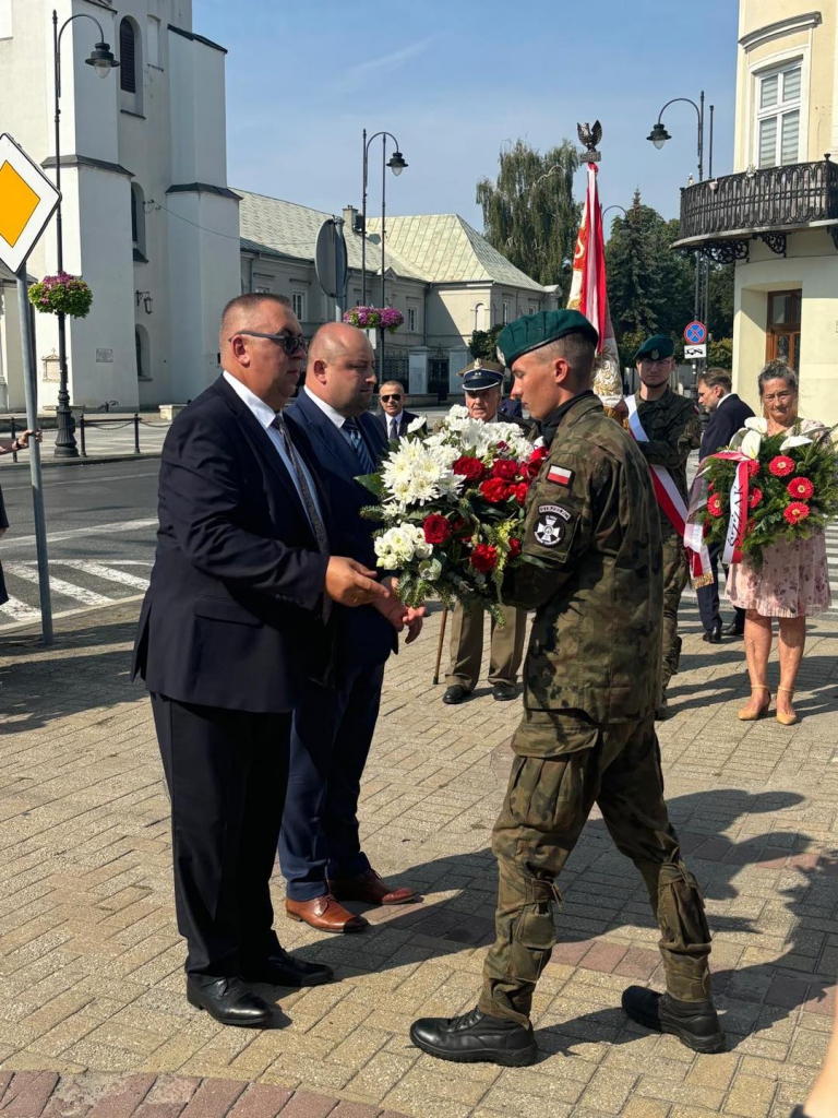 Starosta wraz z Członkiem Zarządu wręczają wiązankę kwiatów młodemu mężczyźnie w mundurze