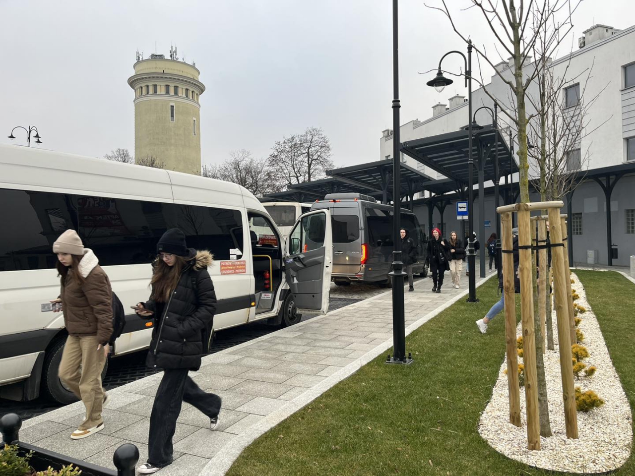 Pasażerowie na terenie Powiatowego Centrum Przesiadkowego Piotrków Trybunalski. W tle Wieża Ciśnień.