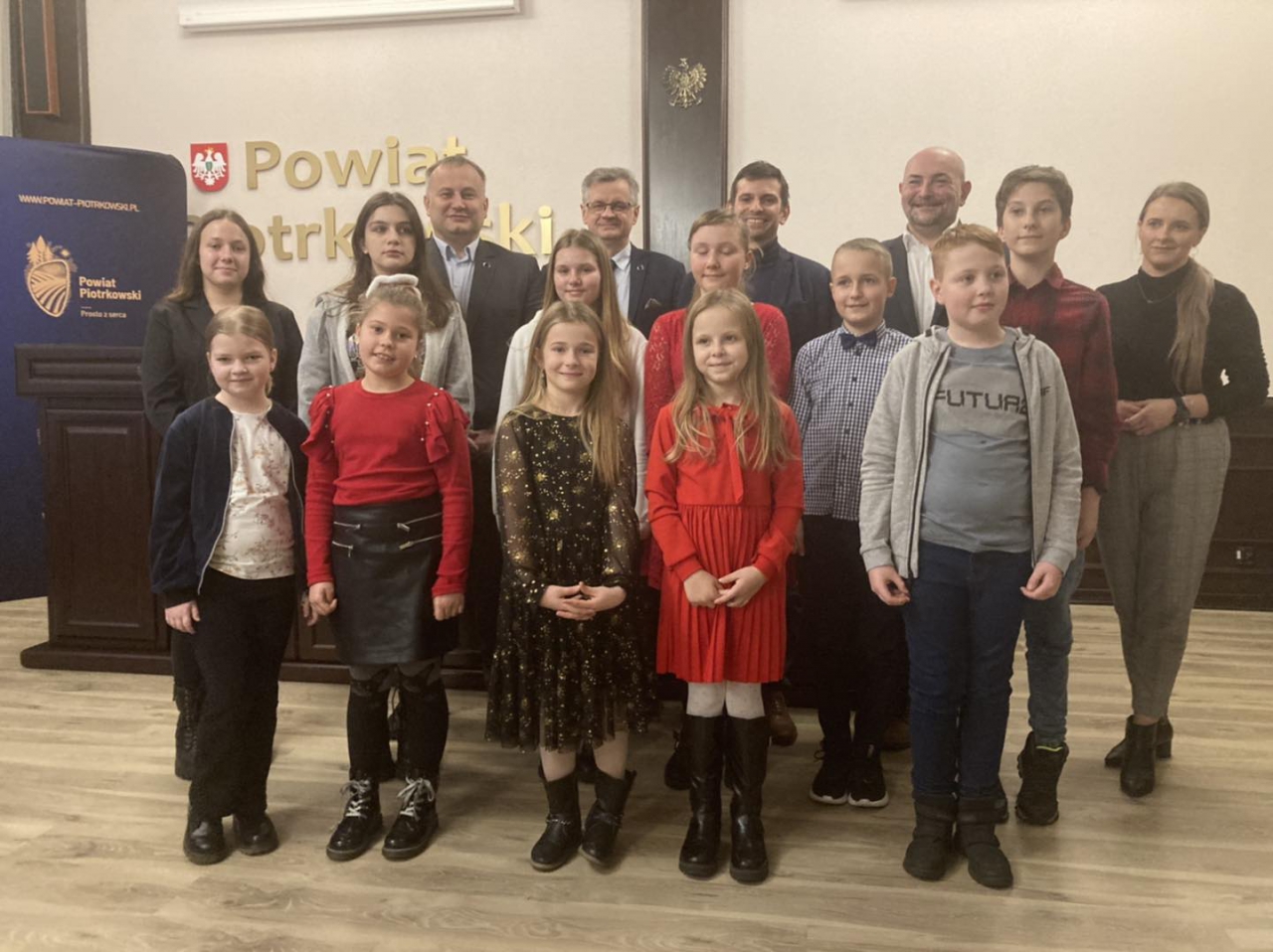 Starosta Piotr Wojtysiak, Wicestarosta Dariusz Magacz, Członek Zarządu Oskar Kuliński oraz przedstawiciel Organizatora stoją z Laureatami Konkursu w Sali konferencyjnej Starostwa. W tle napis powiat piotrkowski.