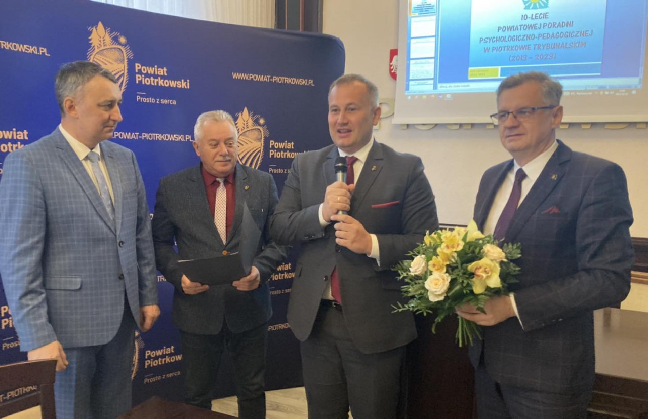 Starosta Piotr Wojtysiak z przedstawicielami władz powiatowych oraz Dyrektorem Poradni znajdują się w sali konferencyjnej Starostwa. W tle logo Powiatu Piotrkowskiego prosto z serca.