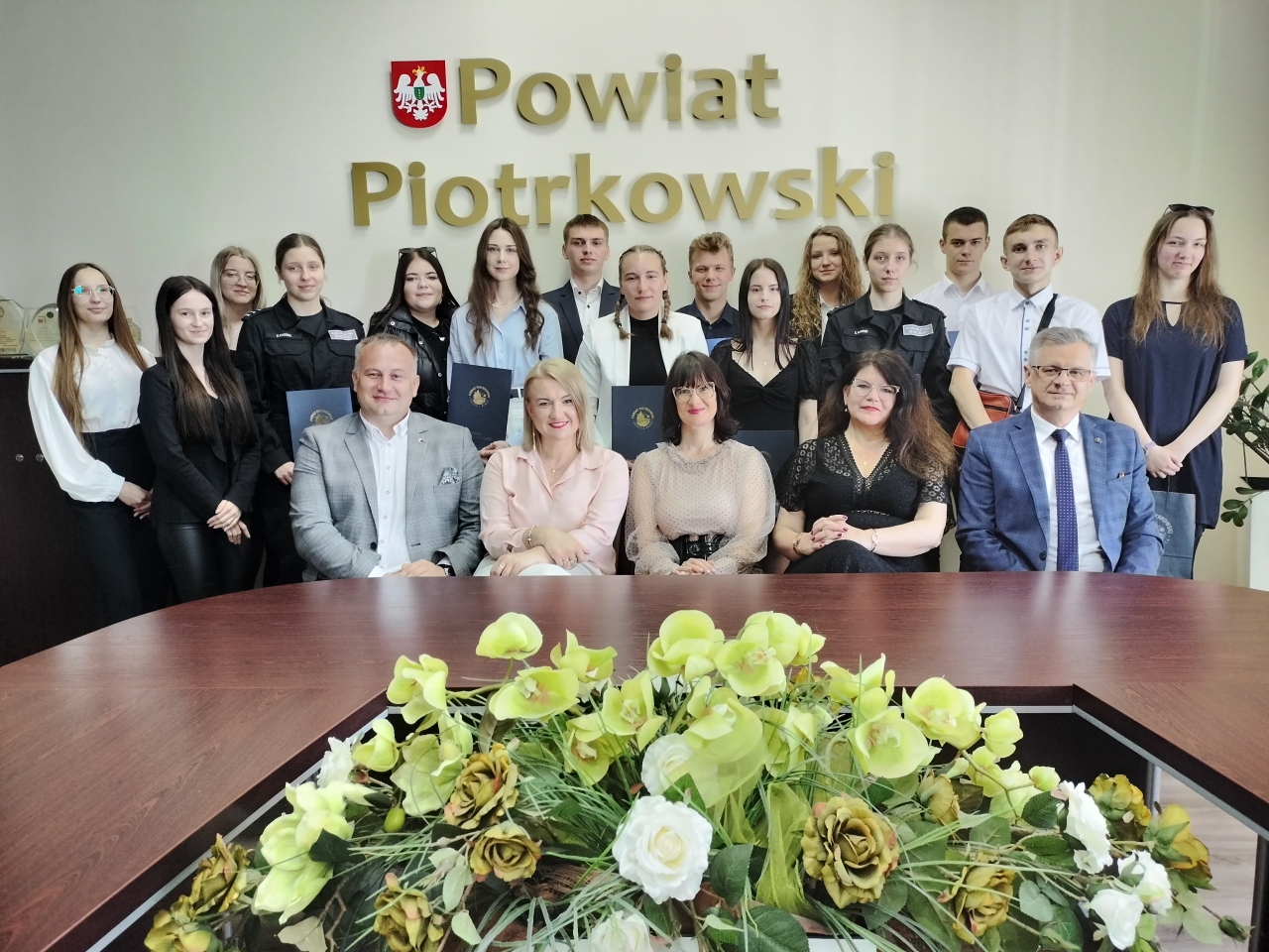Stypendyści stoją w sali Zarządu, przed nimi na krzesełkach siedzą dyrektorzy szkół i Starostowie