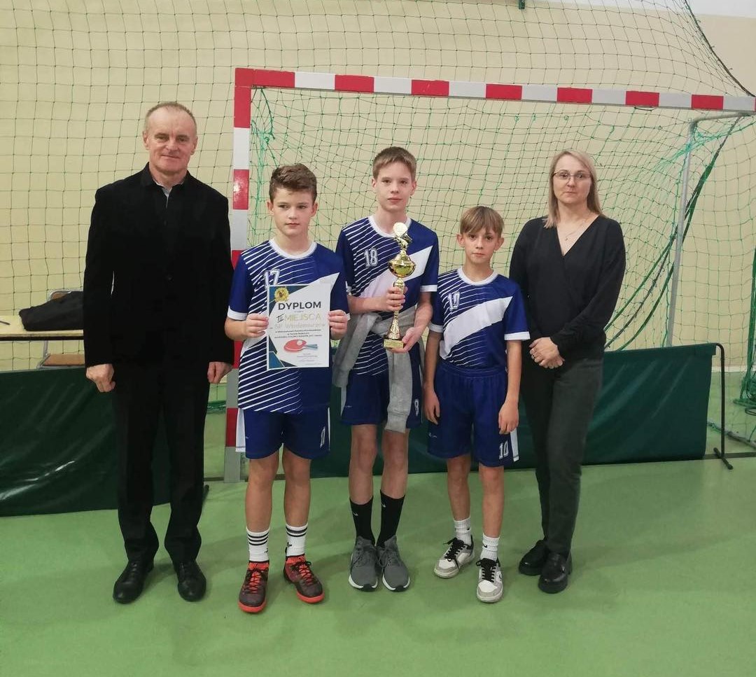 Jedna ze zwycięskich drużyn chłopców stoi w hali sportowej z pucharem