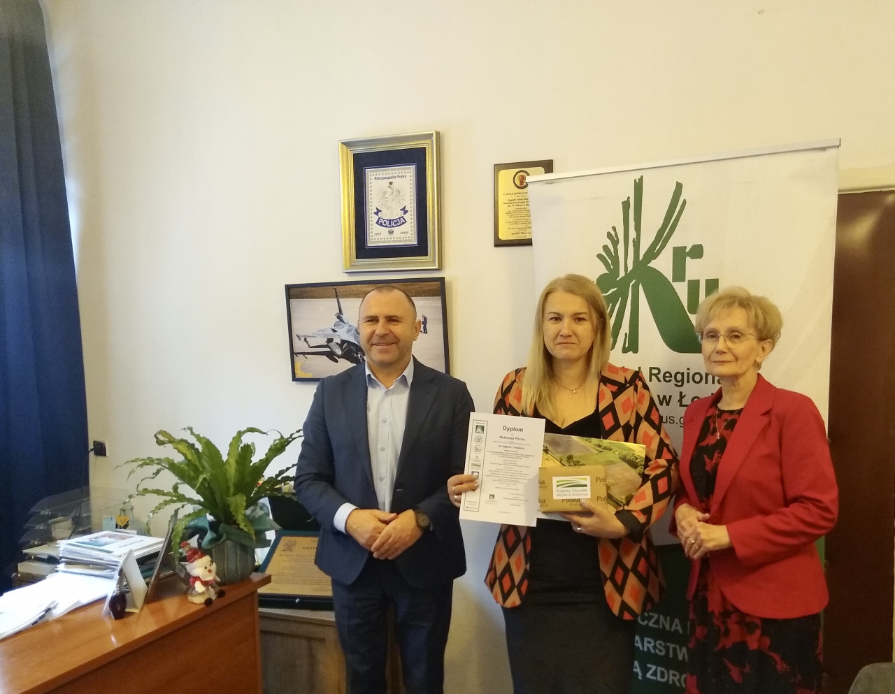 Dyrektor Szkoły w bujnach stoi w gabinecie z dyplomem konkursowym jednego z uczniów.