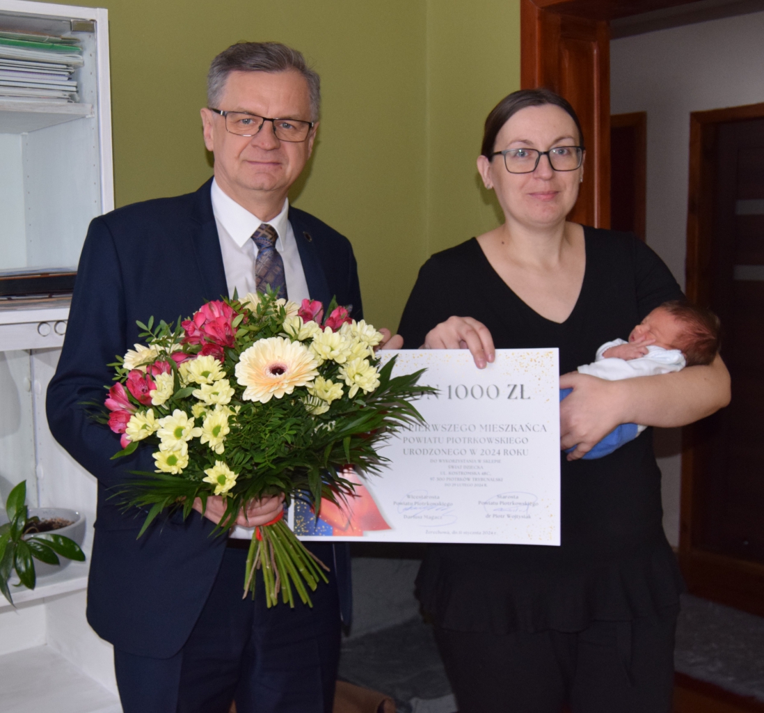 Przedstawiciel Powiatu stoi z mamą trzymająca noworodka na ręku.