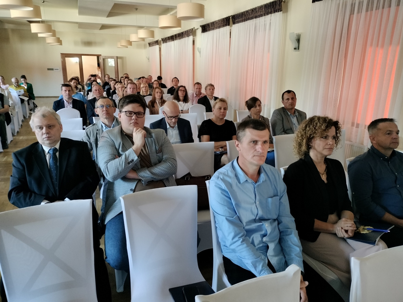 Uczestnicy konferencji geodezyjnej siedzą na krzesłach