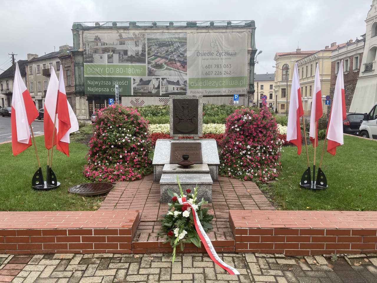 Pomnik, wokół flagi i kwiaty.