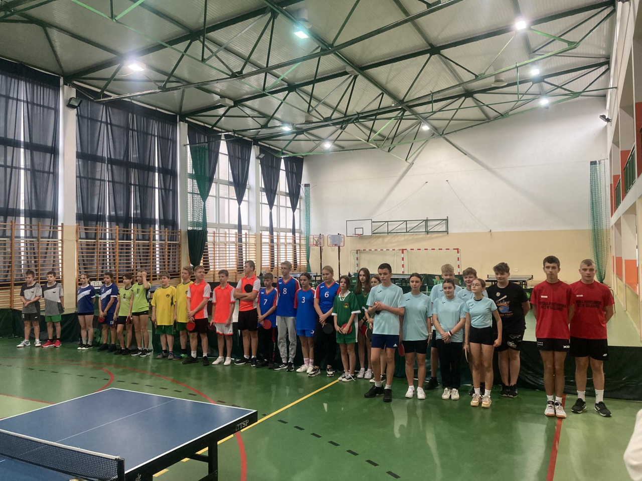 Uczestnicy wydarzenia stoją w hali sportowej