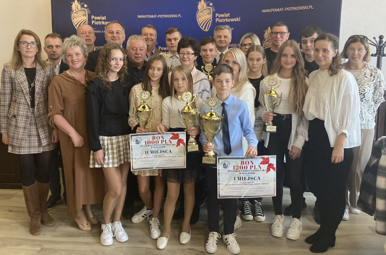 Laureaci podsumowania sportowego z pucharami i bonami pieniężnymi wraz z władzami powiatu, w tle ścianka promocyjna powiatu