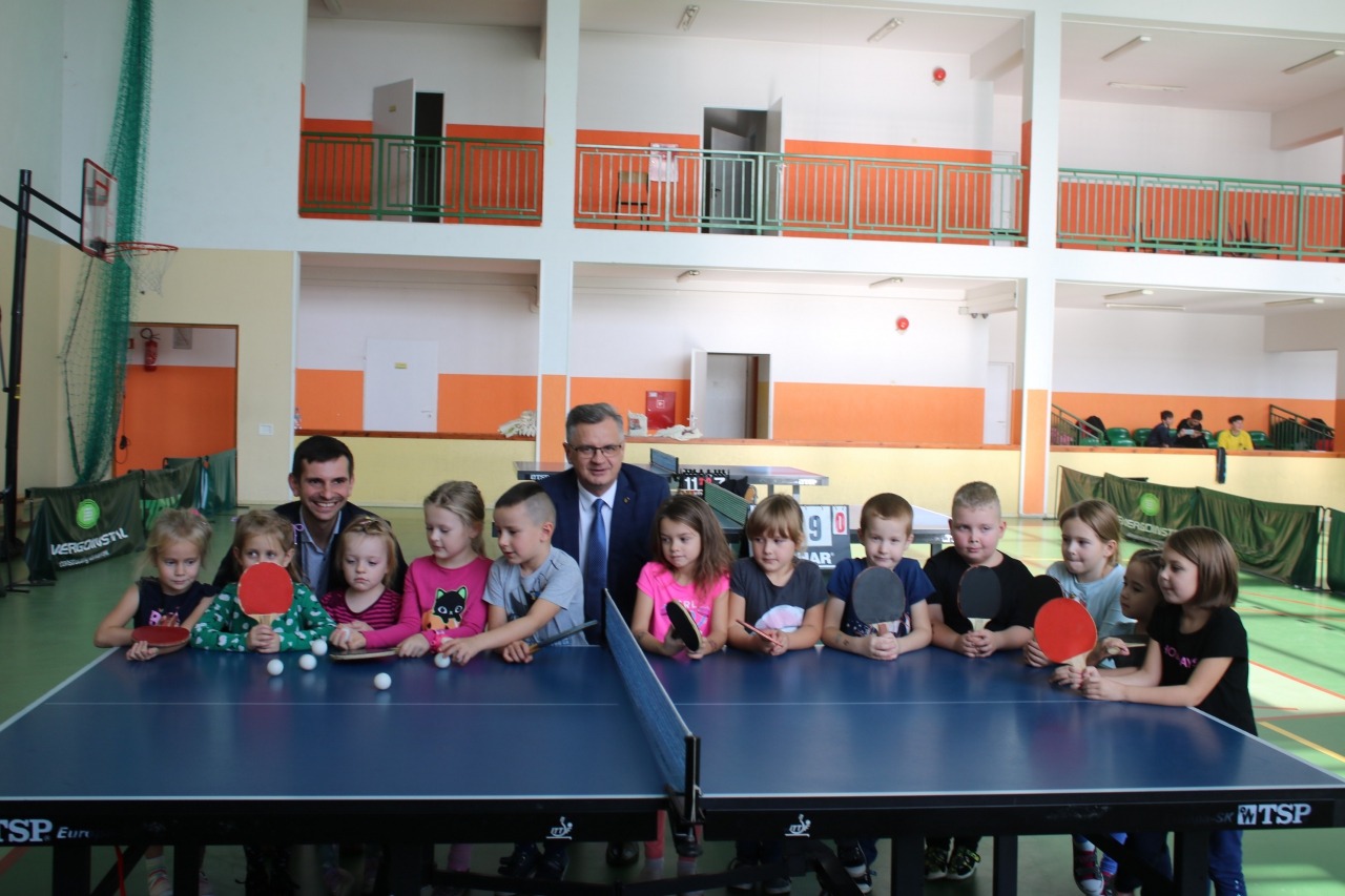 Władze powiatu wraz z dziećmi przy stole tenisowym w hali sportowej