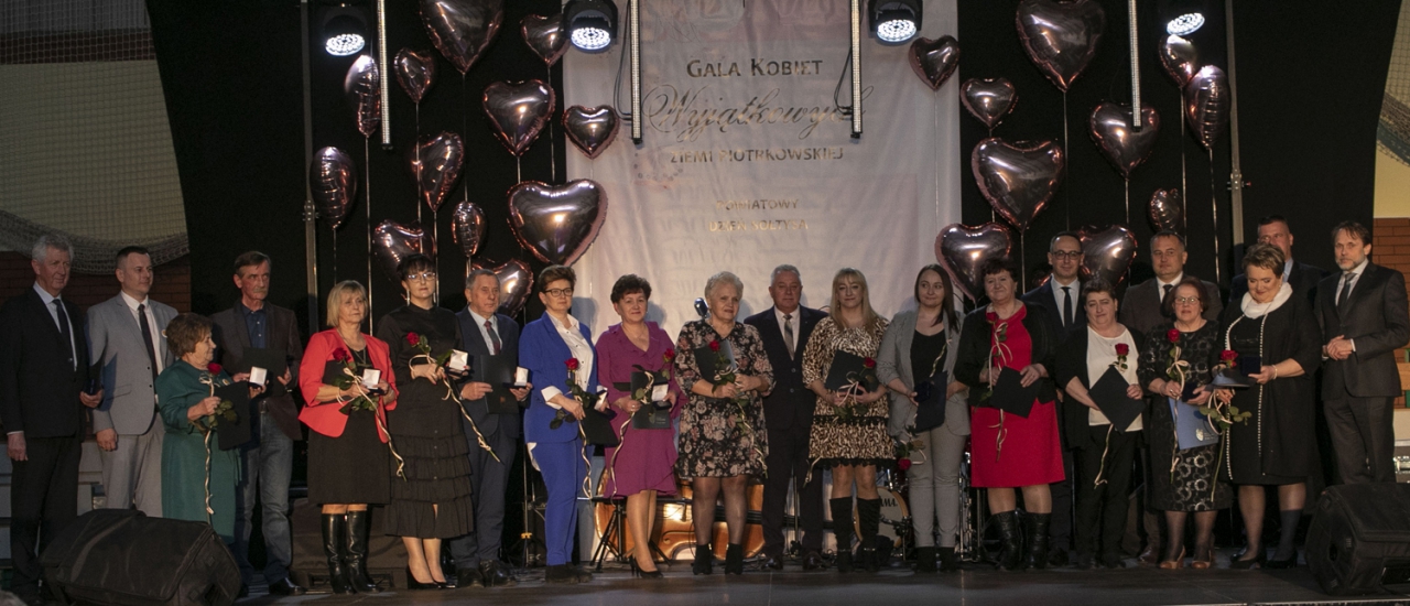 Nagrodzone osoby stoją na scenie w sali w Moszczenicy wraz ze Starostą Piotrem Wojtysiakiem oraz zaproszonymi gośćmi.W tle napis Gala Kobiet Wyjątkowych Ziemi Piotrkowskiej.