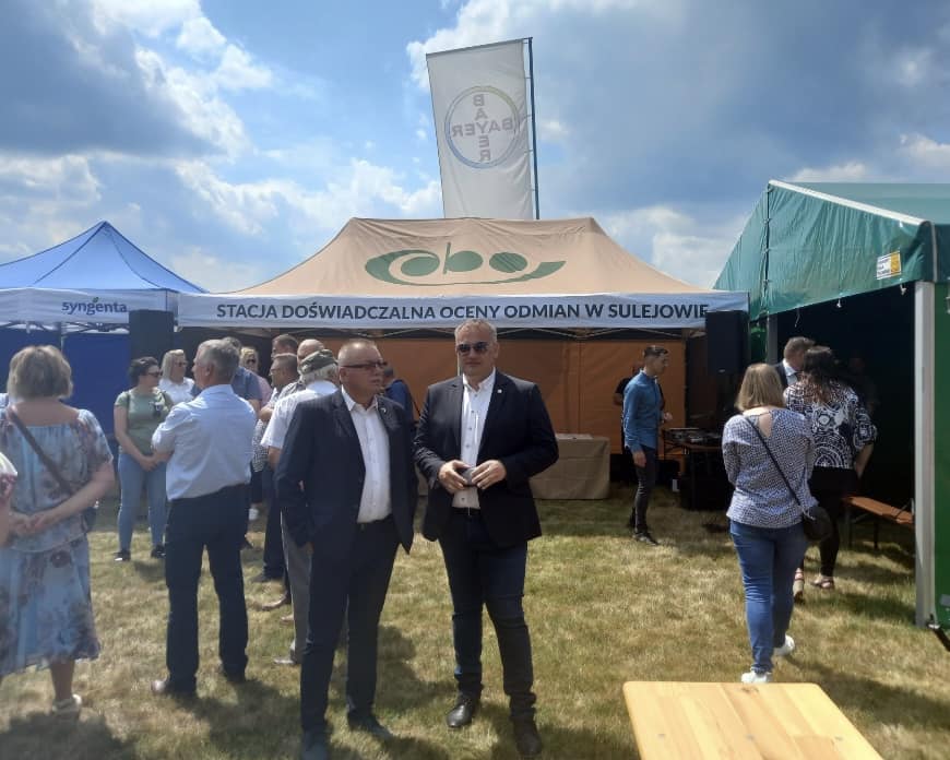 Dwóch mężczyzn stoi, w tle namioty i inni ludzie