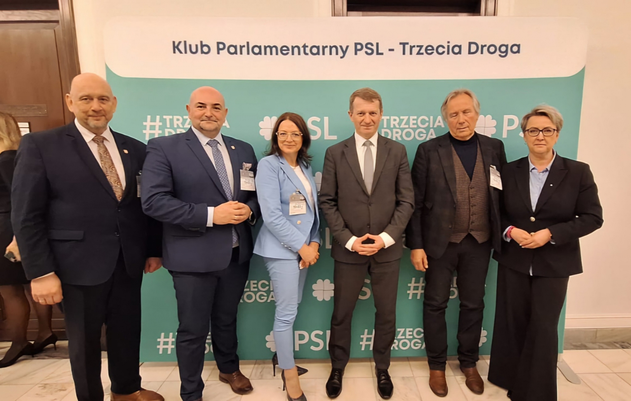 Grupa sześciu osób pozuje na tle ścianki z logo Klubu Parlamentarnego PSL - Trzecia Droga. Wśród uczestników znajdują się przedstawiciele władz powiatowych oraz parlamentarzyści. Wszyscy ubrani elegancko, z identyfikatorami, gotowi do rozmów na temat rozwoju infrastruktury sportowej w regionie