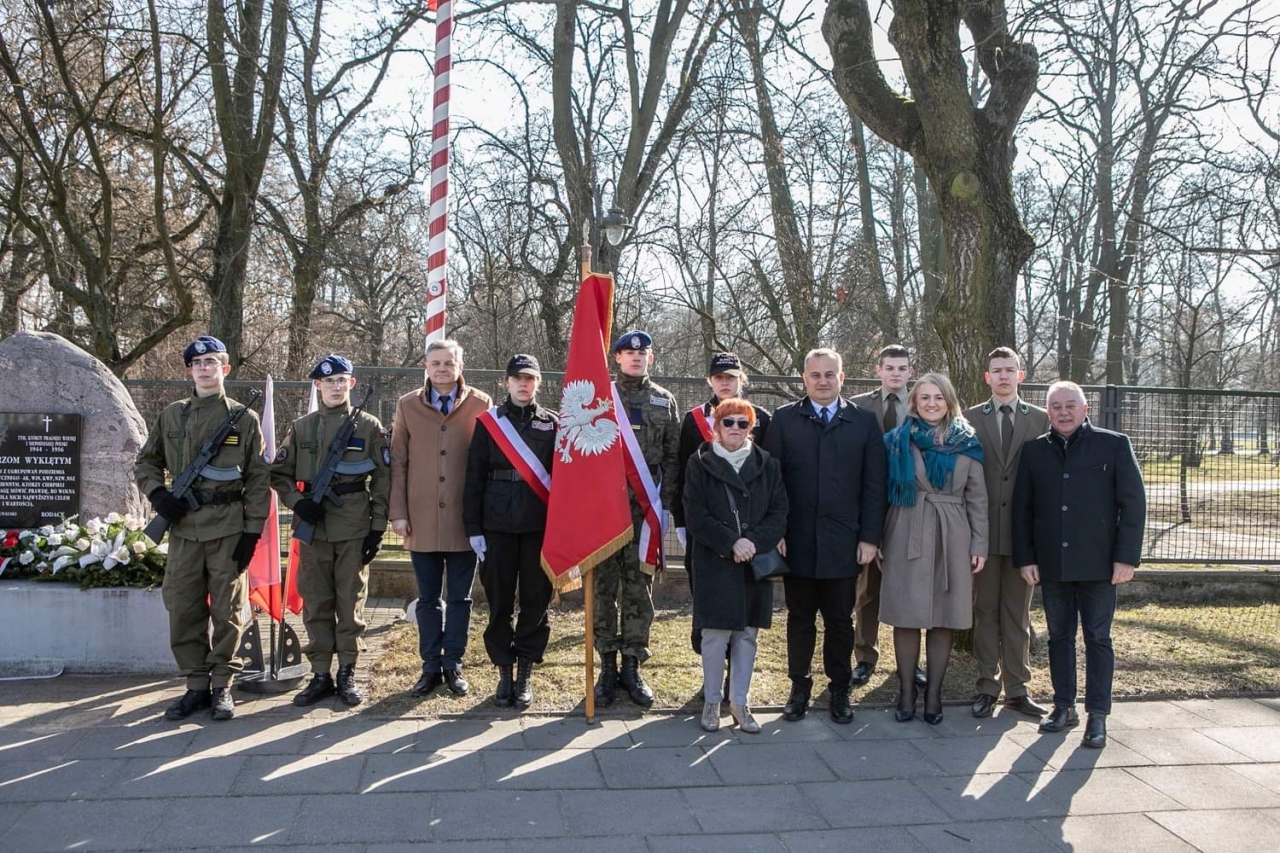 Władze Powiatu stoją przy pomniku Żołnierzy Wykletych w Piotrkowie. W tle park.