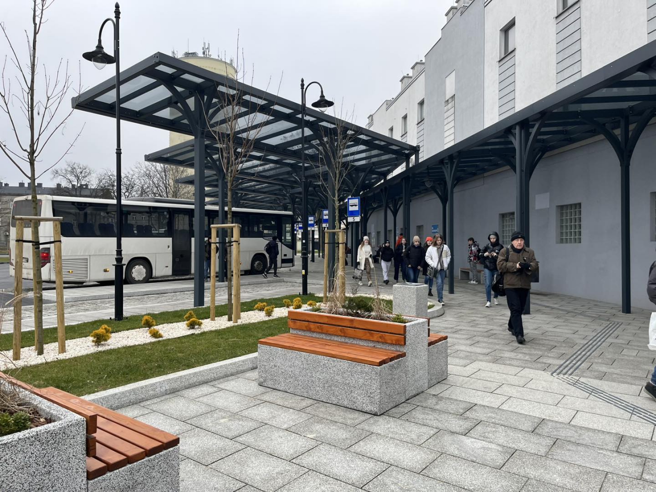Pasażerowie na terenie Powiatowego Centrum Przesiadkowego Piotrków Trybunalski. W tle Wieża Ciśnień.