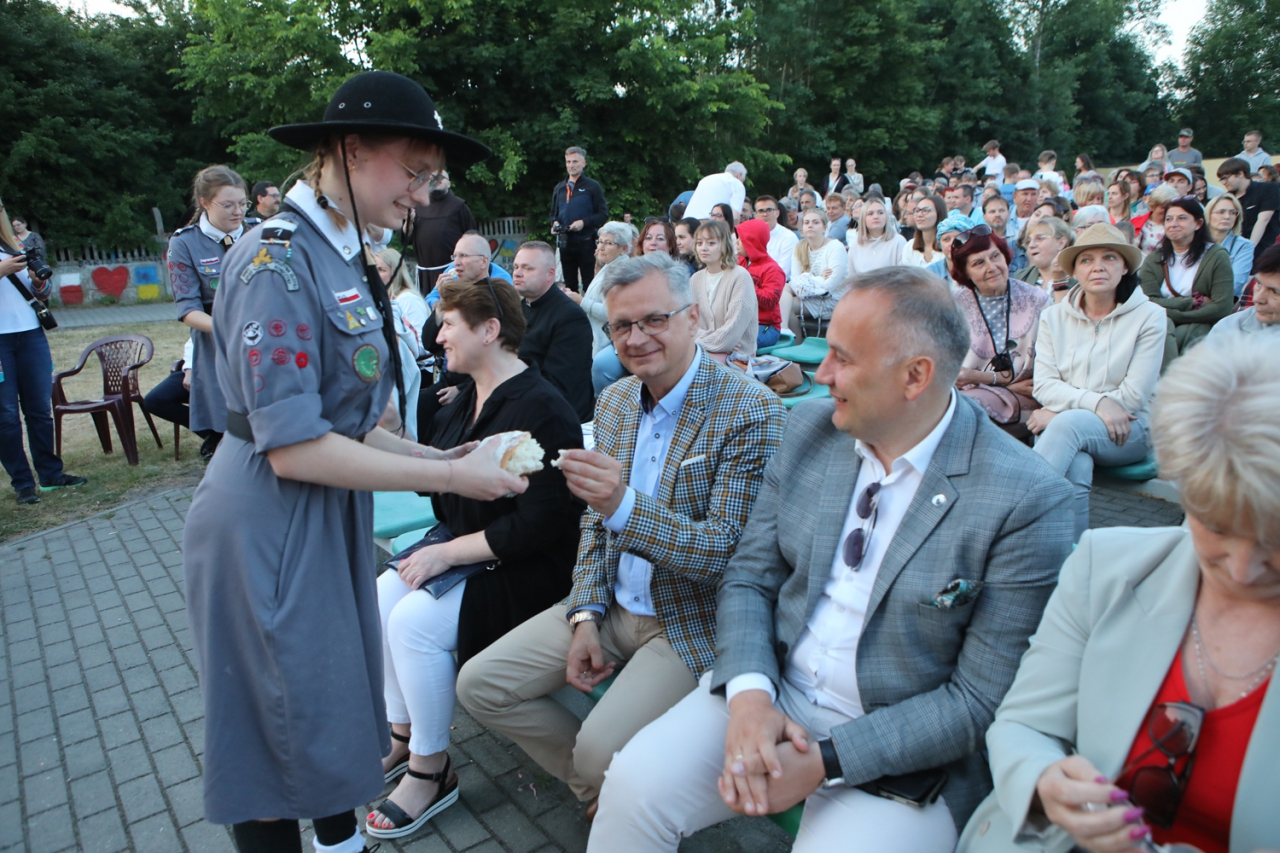 Starosta Piotr Wojtysiak oraz Wicestarosta Dariousz Magacz siedzą na widowni na świeżym powietrzu. W tle pozostali uczestnicy wydarzenia.