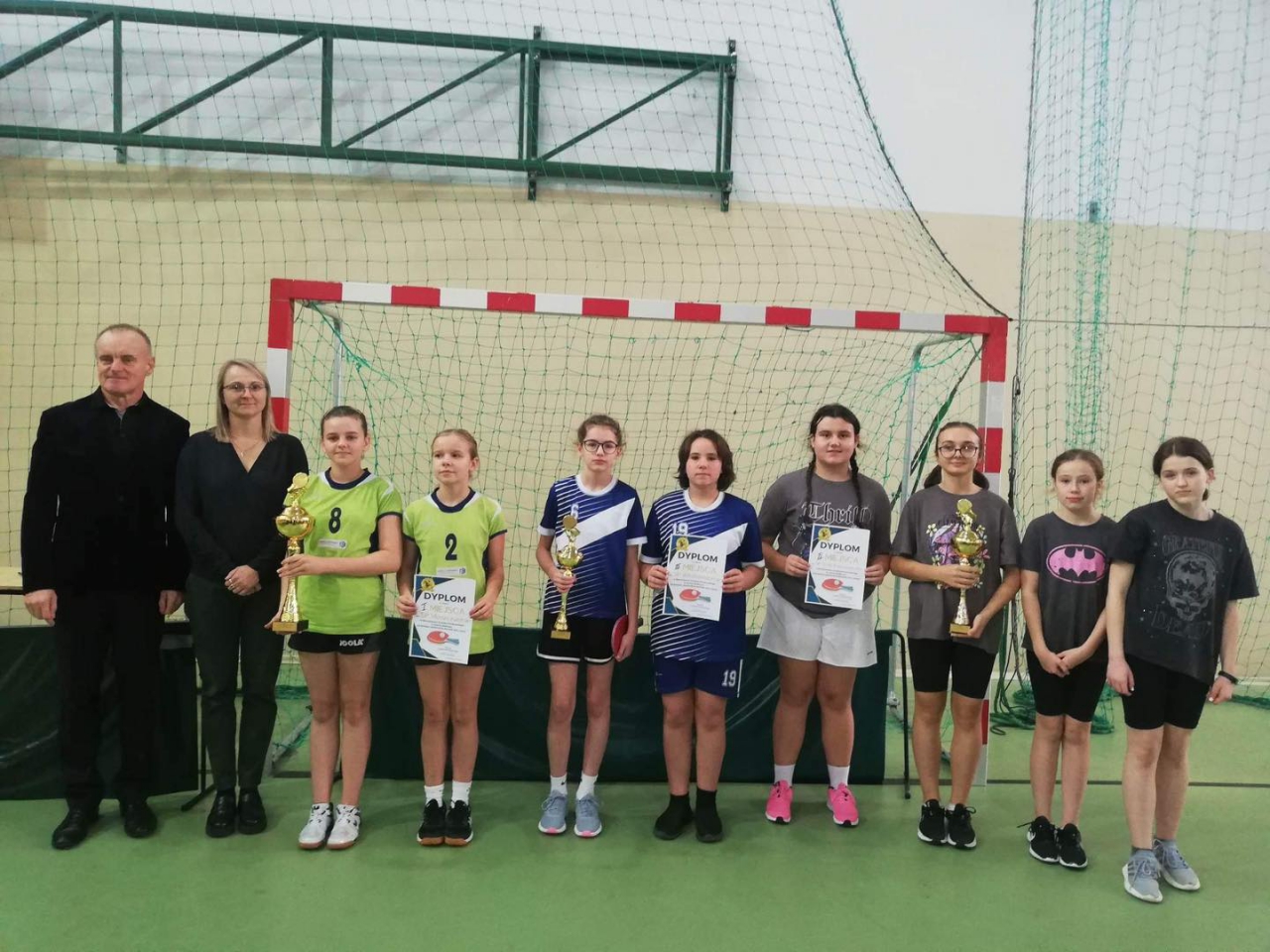 Zwycięskie drużyny dziewcząt stoją w hali sportowej z pucharami