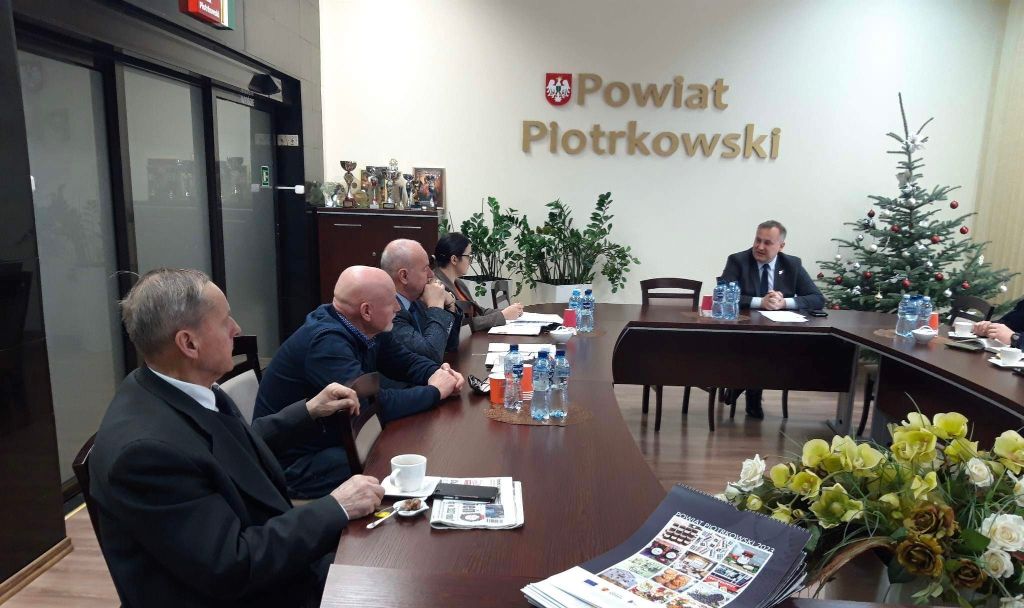 Starosta Piotr Wojtysiak z uczestnikami Komisji znajduje się w sali konferencyjnej Starostwa. w tle napis powiat Piotrkowski.