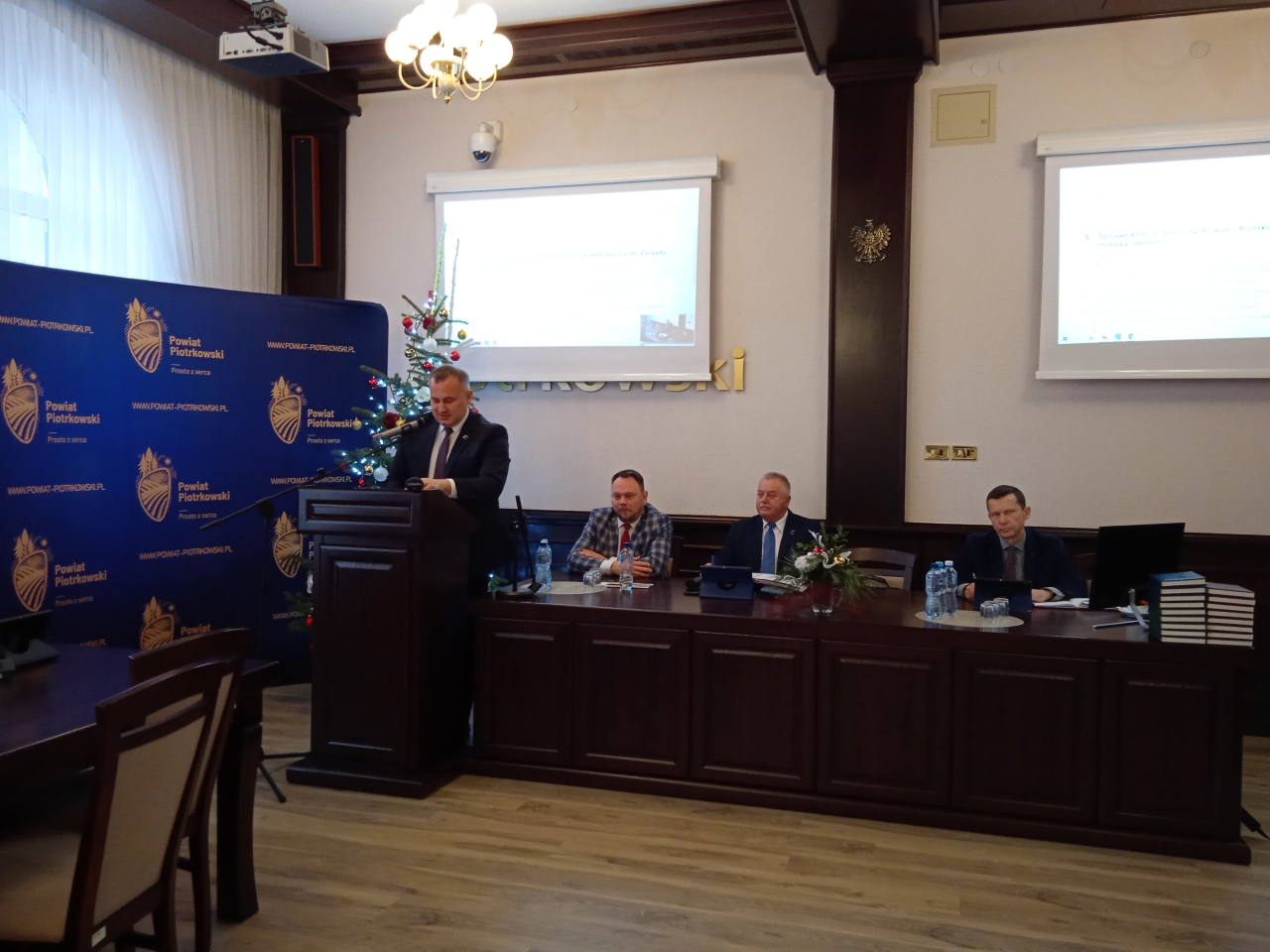 Starosta Piotr Wojtysiak, Przewodniczący Rady oraz Wiceprzewodniczący Rady znajdują się w sali konferencyjnej. W tle napis Powiat Piotrkowski oraz logo Powiatu.