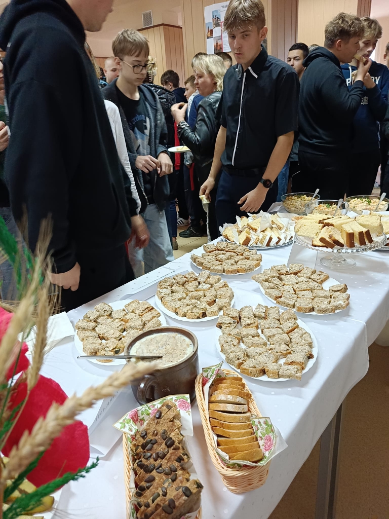 Na stole stoją talerze z ciastem, salaterka ze smalcem, chleb. Obok stołu stoi młodzież