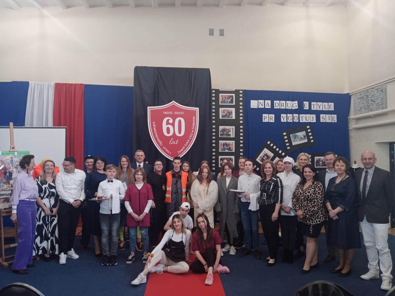 Uczestnicy Jubileuszu stoją na scenie w budynku. W tle napis 60 lat minęło.