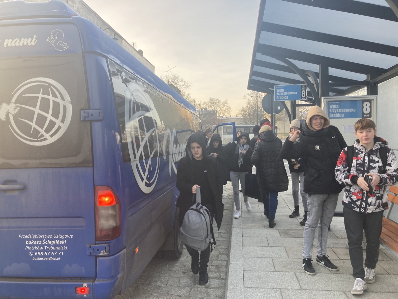 Podróżni na terenie Powiatowego Centrum Przesiadkowego Piotrków Trybunalski obok stoi bus.