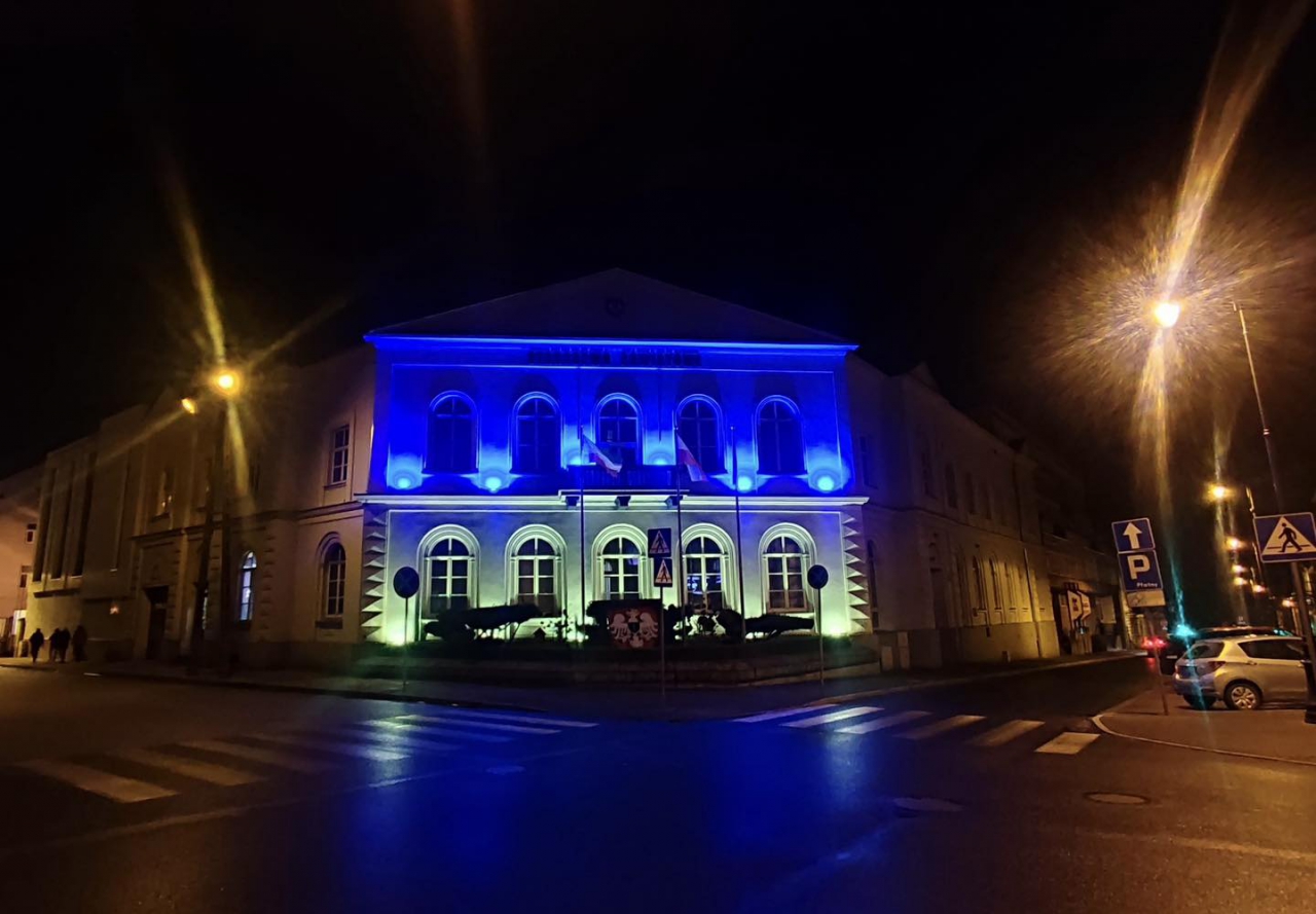 Budynek Starostwa nocą podświetlony na niebiesko i żółto. Widok z zewnątrz.