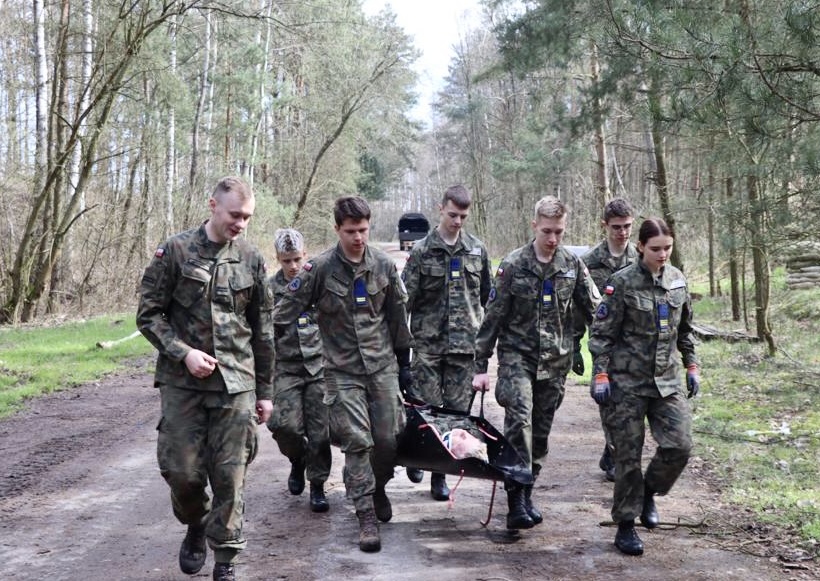 Młodzi chłopcy podczas marszu w lesie, przenoszą rannego